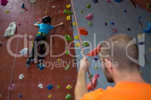 Trainer assisting boy in rock climbing