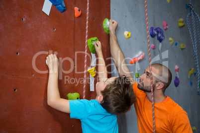 Trainer assisting boy in rock climbing