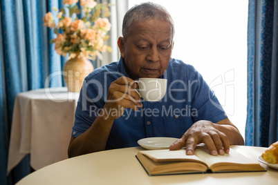 Senior man having drink while reading book in nursing home