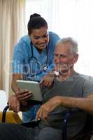 Senior man showing digital tablet to doctor in retirement home