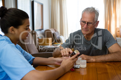 Doctor guiding senior man in taking medicine at table