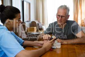 Doctor guiding senior man in taking medicine at table