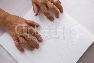 Cropped hands of senior woman reading braille in nursing home