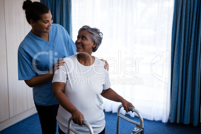 Smiling nurse assisting senior woman in walking with walker