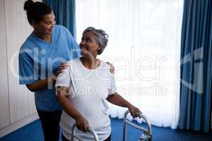 Smiling nurse assisting senior woman in walking with walker