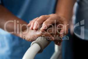 Hands of nurse and senior woman holding walker in nursing home