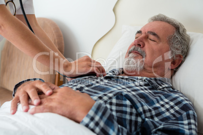 Cropped hands of doctor listening to heartbeats of senior man sleeping on bed