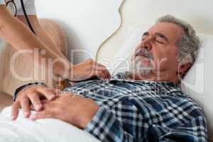 Cropped hands of doctor listening to heartbeats of senior man sleeping on bed