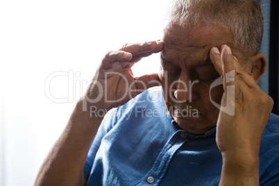 Close up of senior man pressing head while sitting by window