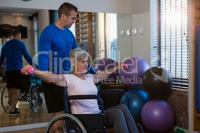 Male physiotherapist helping patient in performing exercise with dumbbell