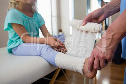 Physiotherapist putting bandage on injured feet of girl patient