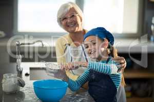 Grandmother posing with granddaughter sieving the flour