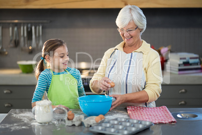 Smiling grandmother showing granddaughter to break eggs