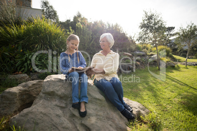 Smiling granddaughter and grandmother using digital tablet in garden