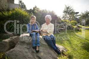 Smiling granddaughter and grandmother using digital tablet in garden