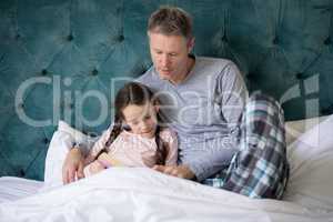 Father and daughter reading book on bed