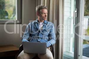 Thoughtful man using laptop on chair