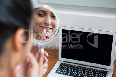 Woman applying lipstick by laptop at home