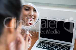 Woman applying lipstick by laptop at home