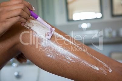 Low section of woman shaving leg