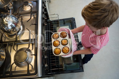 Boy holding muffin tin by oven