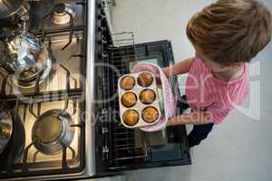 Boy holding muffin tin by oven