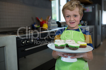 Portrait of boy holding plate with cupcakes