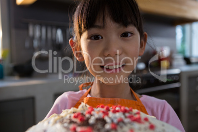 Close-up portrait of girl with cake in kitchen