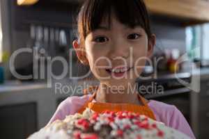 Close-up portrait of girl with cake in kitchen