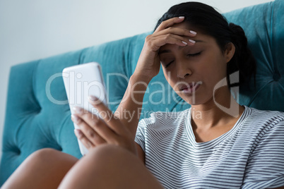 Sad woman holding mobile phone in bedroom