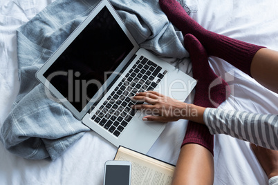 Low section of woman using laptop on bed