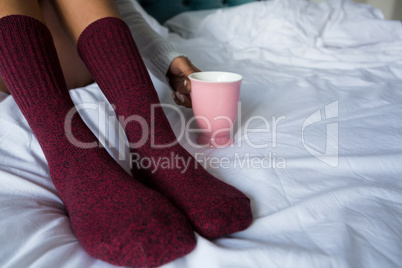 Low section of woman with coffee mug on bed