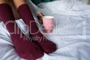 Low section of woman with coffee mug on bed