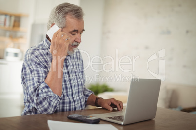Worried senior man taking on phone while using laptop