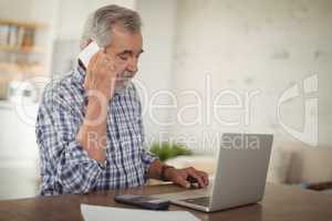 Worried senior man taking on phone while using laptop