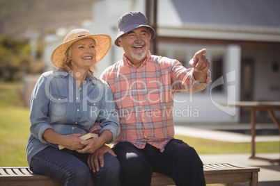 Senior couple pointing at view while sitting on bench