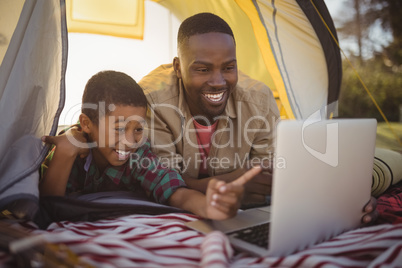 Smiling father and son using laptop in tent