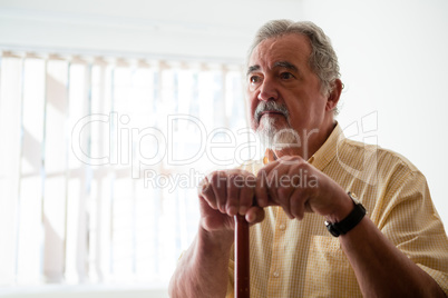 Thougtful senior man looking away while holding walking cane