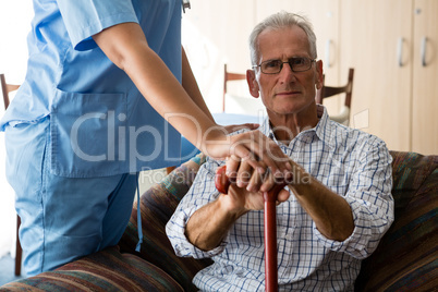 Female doctor standing by senior man sititng on sofa in nursing home