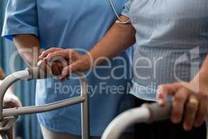 Nurse assisting senior patient in walking with walker at nursing home