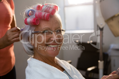 Cropped hands of hairstylist removing curlers from smiling woman hair