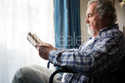 senior man reading book while sitting on wheelchair in nursing home