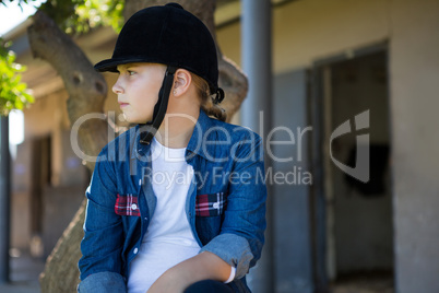 Girl sitting on tree trunk near stable