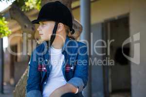 Girl sitting on tree trunk near stable