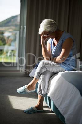 Tense senior woman sitting on bed in bedroom