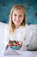 Smiling girl holding breakfast cereal on bed