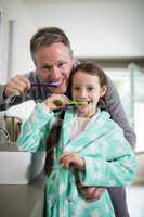 Smiling father and daughter brushing teeth in bathroom