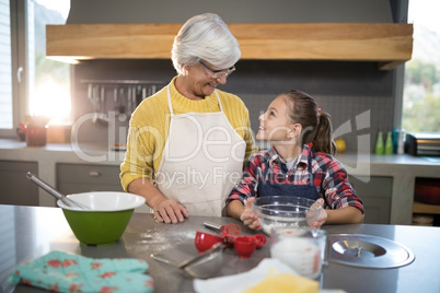 Smiling grandmother and granddaughter looking at each other while holding a bowl of flour