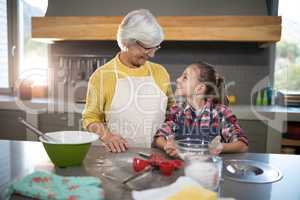 Smiling grandmother and granddaughter looking at each other while holding a bowl of flour