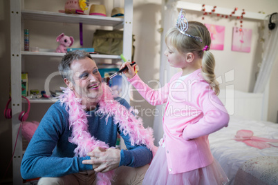 Smiling daughter in fairy costume putting makeup on her fathers face